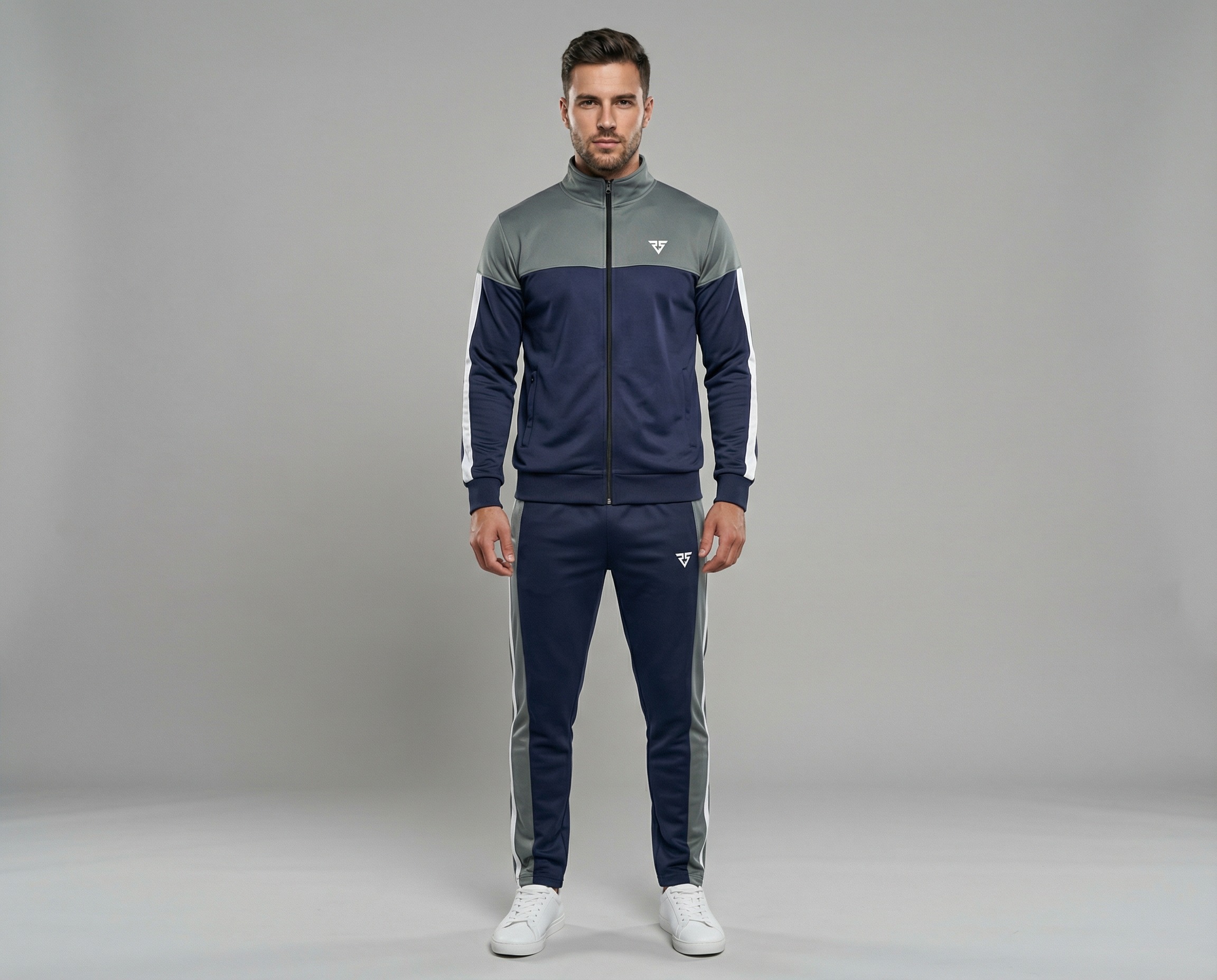 Man wearing a navy blue and grey contrast panel tracksuit with white sleeve stripes, full-zip jacket and tapered pants