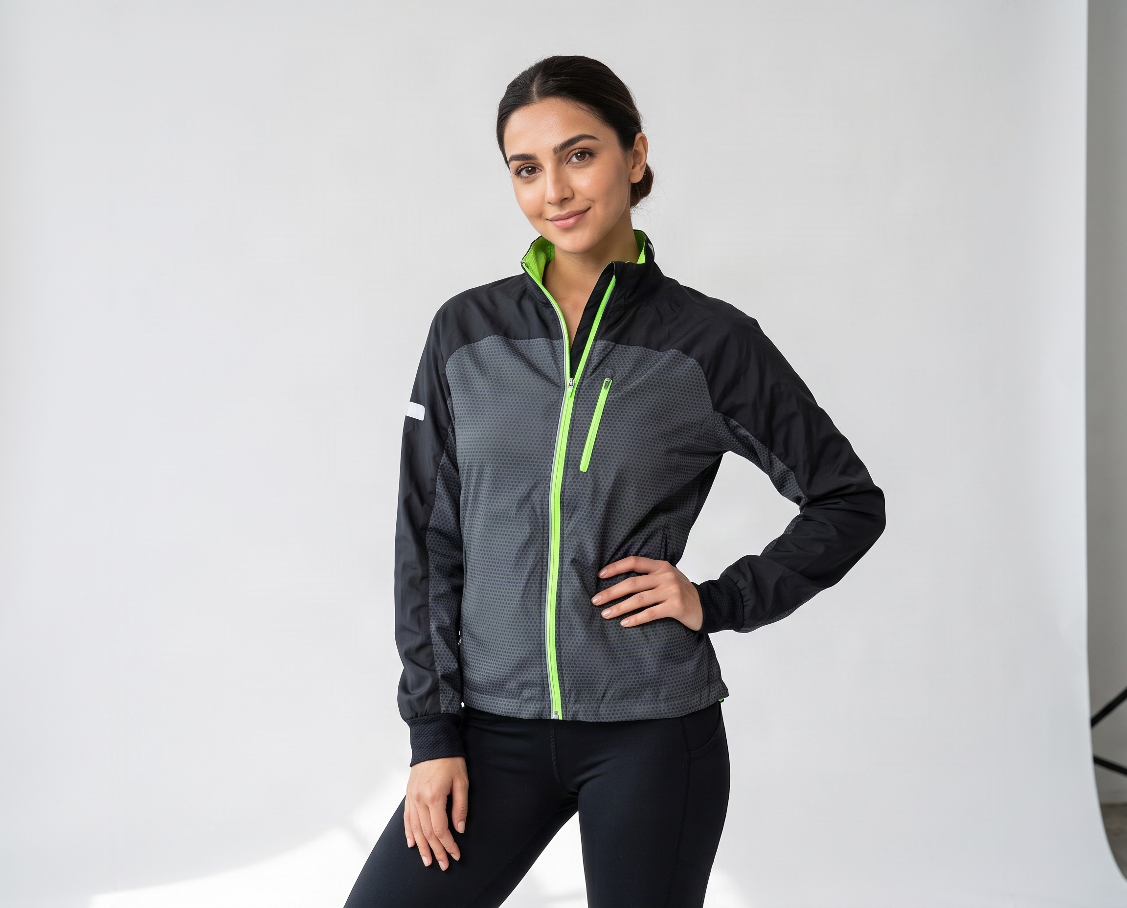 Woman wearing a black and grey full-zip training jacket with fluorescent green zipper, stand-up collar and chest pocket